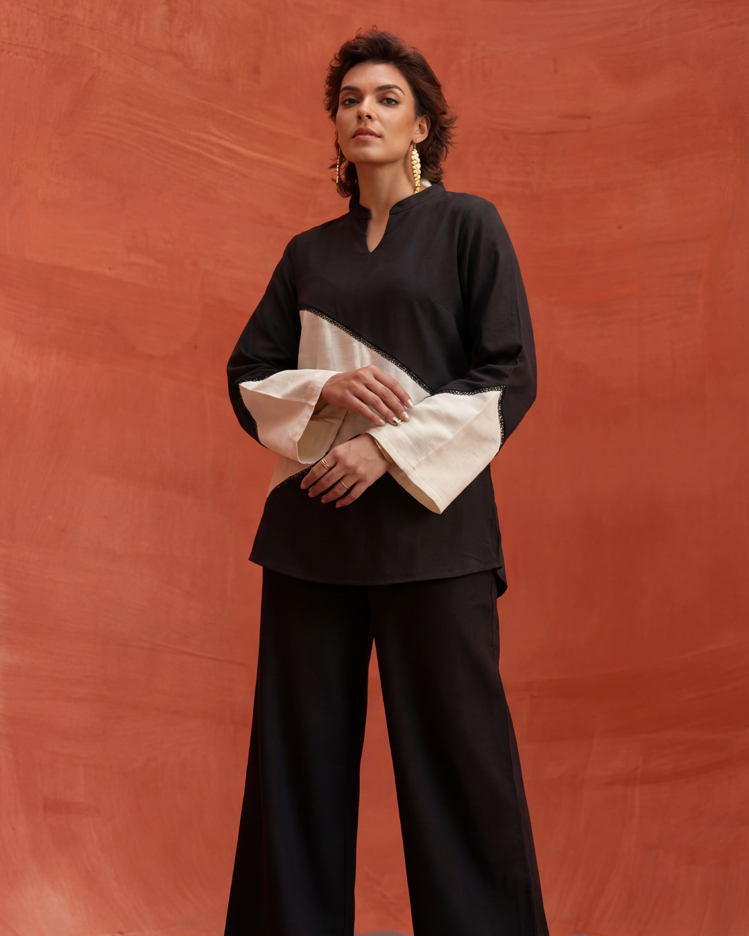 M'PALATH black bell-sleeve top with cream accents against terracotta backdrop